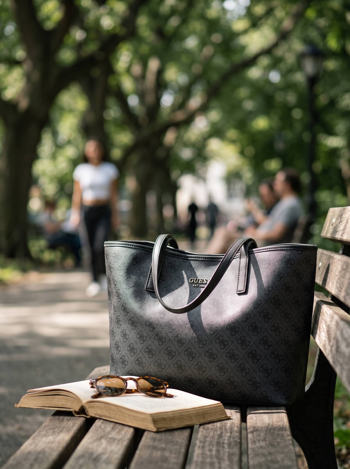 Сумка Guess на парковой скамейке рядом с книгой и очками